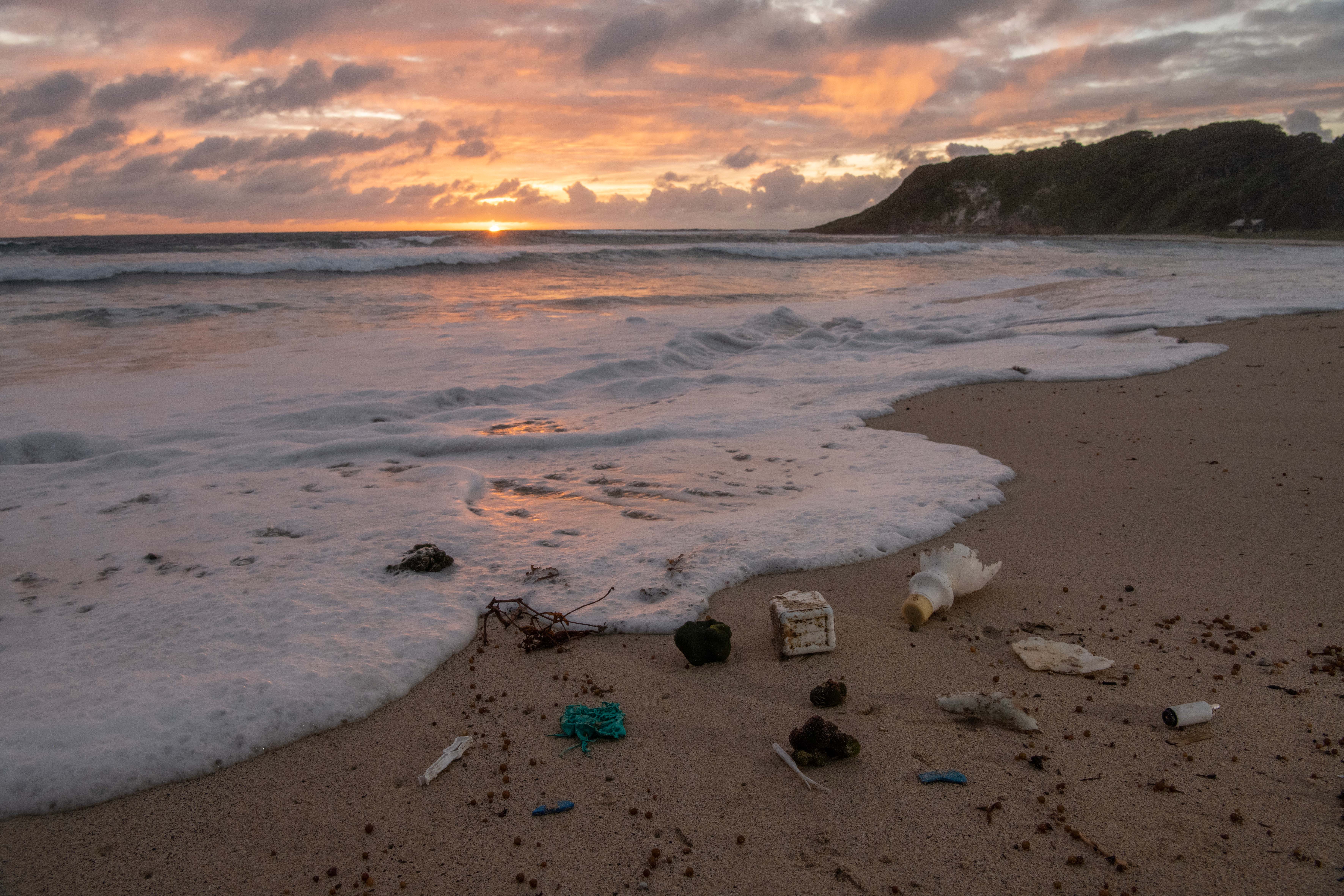 A beach with golden sand littered with bits of ocean plastic washing up. 